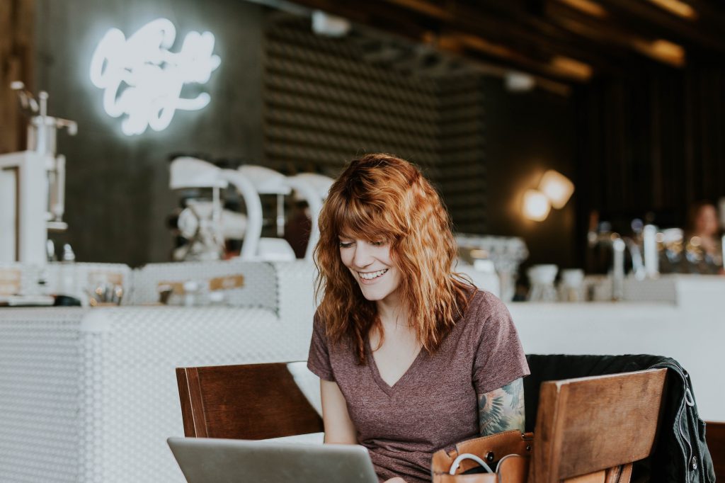 Women working in a cafe, smiling at her laptop